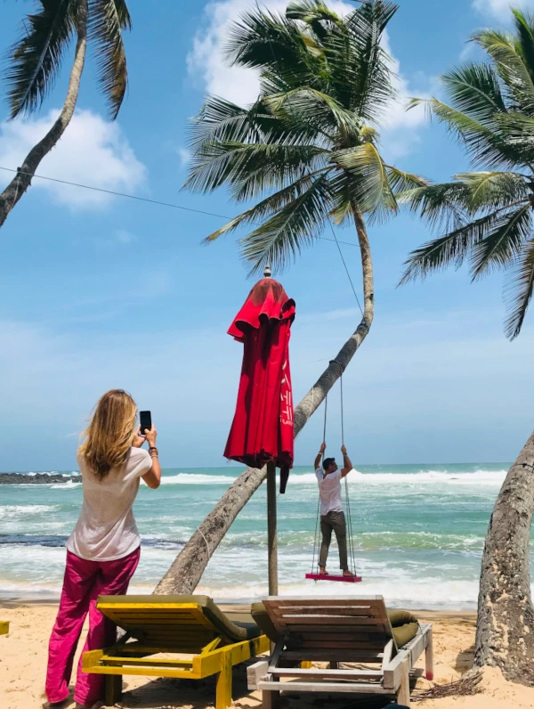 Couple on a tropical sri lankan beach. Man on the swing. Lady taking the picture